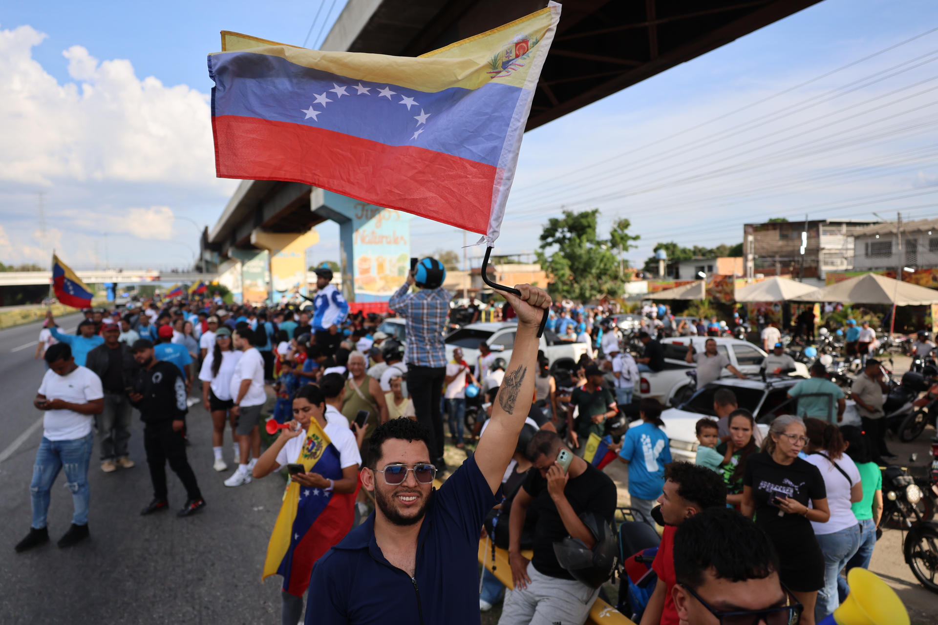 Miles reciben la caravana encabezada por María Corina Machado tras su esperado regreso a Venezuela — AME9766. MARACAY (VENEZUELA), 25/10/2026.- Una mujer sostiene una bandera mientras espera la llegada de la líder opositora y premio nobel de la paz 2025 este domingo, en Maracay (Venezuela). EFE/ Miguel Gutiérrez